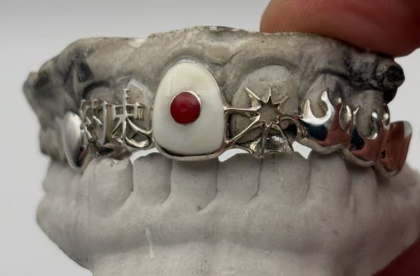 Silver grill with kanji, a red stone, star and flame cutouts